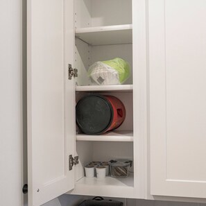 Ein weißes Schranksystem mit Regalen, das eine Plastiktüte, einen roten Behälter und kleine weiße Behälter enthält.
