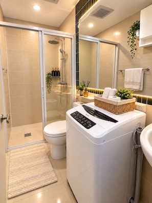 Un baño moderno con ducha envuelta en vidrio, inodoro, lavadora y lavamanos.