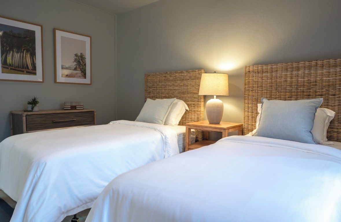 A hotel room with two beds, a nightstand with a lamp, and two framed pictures on the wall.