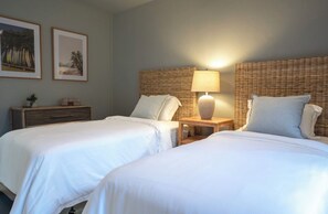 Een hotelkamer met twee bedden, een nachtkastje met een lamp en twee ingelijste foto's aan de muur.