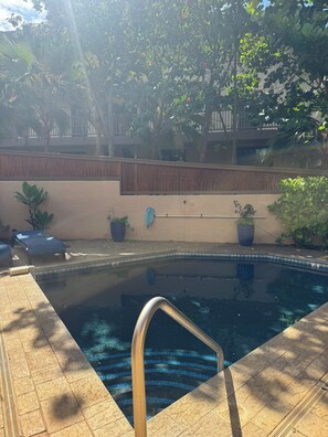 A swimming pool with a metal ladder, surrounded by potted plants and a wooden fence. - Poipu Makai Luxury Oceanfront Condo with AC & Sunset Views (Koloa)