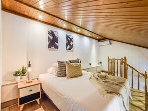 A bedroom with a wooden ceiling, a bed with white bedding, a nightstand, a lamp, and a staircase. - Penthouse With Terrace, Plaza Espana (Madrid)