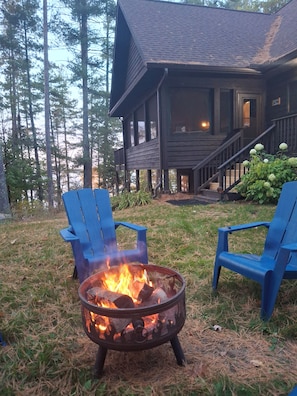 A wooden cabin with a fire pit in the yard, surrounded by tall trees. - Spacious Lakehouse on Lac Courte Oreilles (Stone Lake)