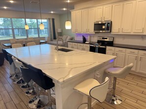 A modern kitchen with a large island, bar stools, and a dining area with chairs. - Spacious 7-bedroom house in welcoming Kissimmee with AC (Kissimmee)