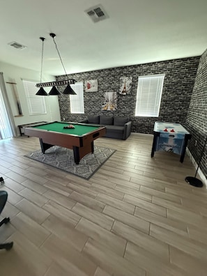A room with a pool table, a sofa, and a brick wall. - Spacious 7-bedroom house in welcoming Kissimmee with AC (Kissimmee)