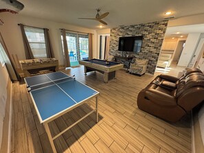 A room with a foosball table, pool table, leather recliner, and a flat-screen TV mounted on a brick wall. - Spacious 7-bedroom house in welcoming Kissimmee with AC (Kissimmee)