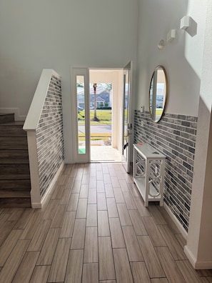 A hallway with a wooden floor, a white bench, and a door leading outside. - Spacious 7-bedroom house in welcoming Kissimmee with AC (Kissimmee)