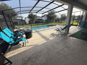 A covered outdoor area with a pool, lounge chairs, and a table. - Spacious 7-bedroom house in welcoming Kissimmee with AC (Kissimmee)