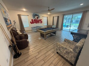 A pool table in a living room with a sofa and a pool cue rack. - Spacious 7-bedroom house in welcoming Kissimmee with AC (Kissimmee)