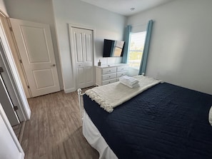 Un dormitorio con cama, cómoda, televisor y puerta.