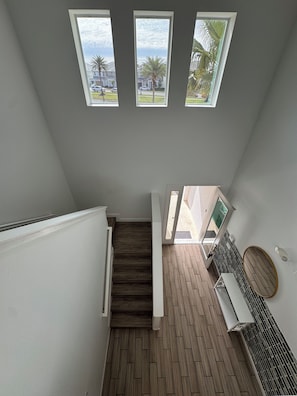 Una escalera con escalones de madera que lleva a un rellano con baranda blanca y vistas al exterior.
