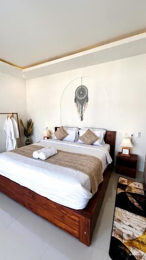 A neatly made bed with a wooden frame, a bedside table with a lamp, and a wall-mounted decorative item. - Batur essence villa by mount batur (Bangli)