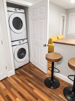 A laundry room with two stacked washing machines, a wooden floor, and a yellow sofa in the adjacent living area. - 2-br apt 2.5 bath in New Haven near Downtown and Yale Hospital - Free parking (New Haven)
