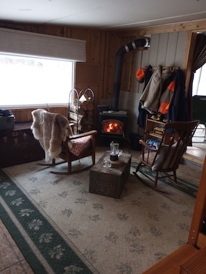 A cozy room with a wood-burning stove, rocking chairs, and a window with a view.