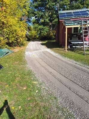 A gravel driveway leading to a red building with solar panels on the roof. - Beautiful cabin in soothing Livonia perfect for a relaxing getaway. Off grid . (Livonia)