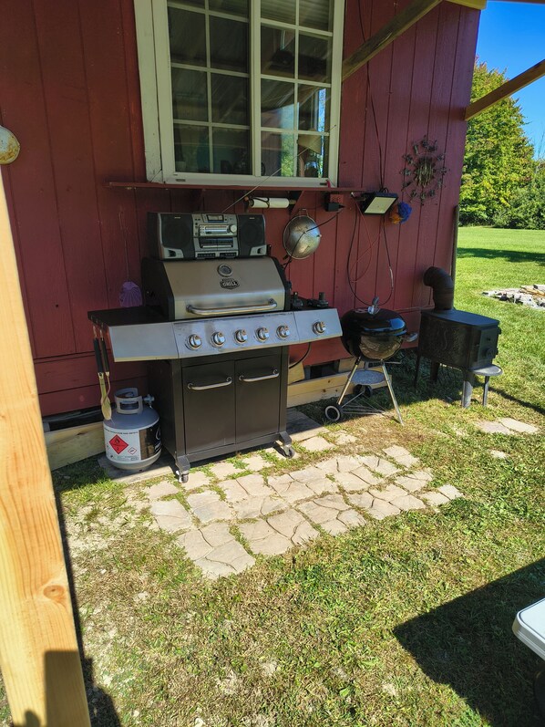 Una parrilla de gas portátil con un quemador lateral y un horno incorporado, ubicada en un patio de piedra frente a un edificio rojo.