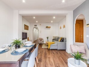 A modern living room with a grey sofa, a pink armchair, and a dining area with a table set for four. - Spacious Apartment Near Retiro Park (Madrid)