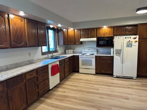 A kitchen with wooden cabinets, a white stove, a microwave, and a refrigerator. - The Coteau Chateau 3-bedroom country home near Conde awaits you (Conde)