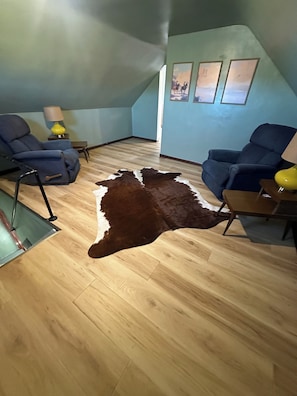 A room with a wooden floor, two blue armchairs, a brown and white leather rug, and a lamp on a side table. - The Coteau Chateau 3-bedroom country home near Conde awaits you (Conde)