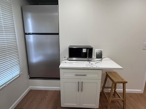 A compact kitchen with a stainless steel refrigerator, a microwave, and a small wooden stool. - Modern Luxury 1BR Walk to Pitt, CMU & UPMC (Pittsburgh)