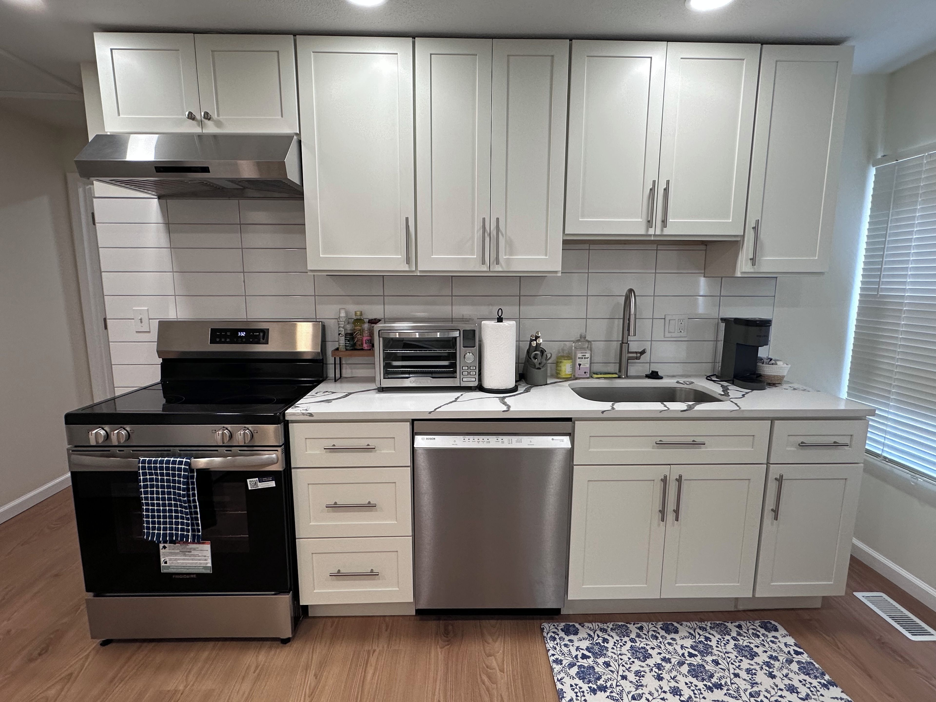 A modern kitchen with white cabinets, stainless steel appliances, and a patterned rug.