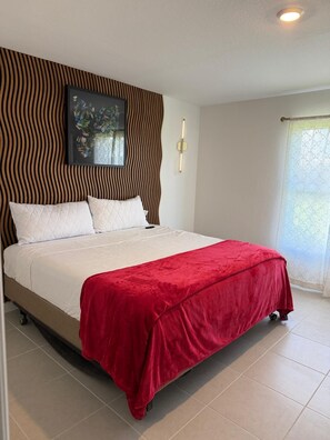 A neatly made bed with a red blanket, a wall-mounted light fixture, and a framed picture above the bed. - Golden Pine Haven, Luxury 5-Bedroom Vacation Home. (Homestead)