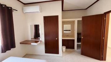 Habitación de hotel con cama, escritorio pequeño, aire acondicionado, espejo y baño con lavabo y espejo.