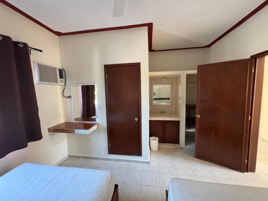 A hotel room with a bed, a small desk, a mirror, a wardrobe, and a bathroom visible through an open door.