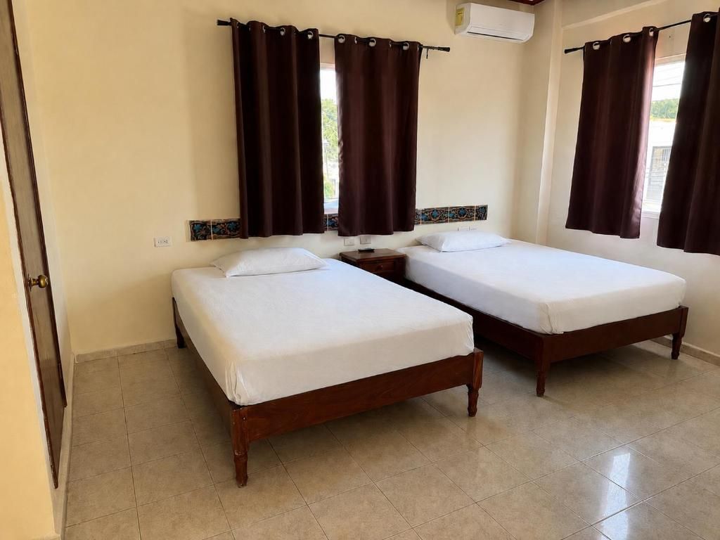 Una habitación con dos camas de madera, una mesita de noche y una ventana con cortinas.