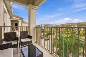 A balcony with wicker furniture and a glass table, overlooking a residential area with palm trees and parked cars. - 3BR Vista Cay, Conventions, Parks and Orlando Fun (Orlando)