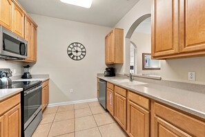 A kitchen with wooden cabinets, a stainless steel oven, a microwave, a coffee maker, and a clock on the wall. - 3BR Vista Cay, Conventions, Parks and Orlando Fun (Orlando)