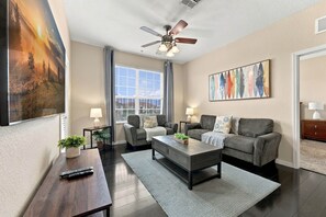 A modern living room with a sofa set, a coffee table, a TV, and a ceiling fan. - 3BR Vista Cay, Conventions, Parks and Orlando Fun (Orlando)