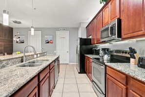 A modern kitchen with granite countertops, stainless steel appliances, and wooden cabinets. - 3BR close to Convention Center and Theme Parks (Orlando)