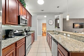 A modern kitchen with wooden cabinets, stainless steel appliances, granite countertops, and a large clock on the wall. - 3BR close to Convention Center and Theme Parks (Orlando)