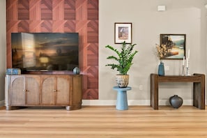 Ein Wohnzimmer mit Fernseher, Schrank, Pflanze, Vase und einem Bildrahmen an der Wand.