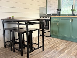 A kitchen with a wooden table and stools, a stove, and green cabinets. - Peaceful Mountain Retreat Near Durango with Beautiful Nature Views (Bayfield)