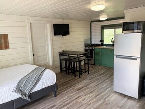 A compact room with a bed, a small dining table, a kitchen area with a microwave, stove, and green cabinets. - Peaceful Mountain Retreat Near Durango with Beautiful Nature Views (Bayfield)