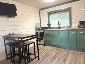Een keuken met een houten tafel, barkrukken, een fornuis en groene kastjes.