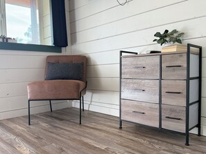 Een hoekappartement met een bruine leren fauteuil, een houten kast met lades, en een raam met gordijn.
