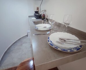 Mesa de jantar posta com pratos, talheres e taças de vinho, com uma cozinha ao fundo.