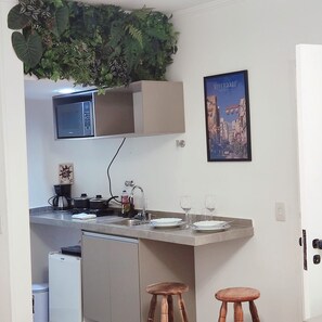 A compact kitchen with a microwave, a coffee maker, and a sink. There are two stools and a framed picture on the wall. - Apart Beautiful Sky, Feirinha Liberdade São Paulo (São Paulo)