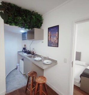 A compact kitchen with a built-in fridge, a sink, and two wooden stools. - Apart Beautiful Sky, Feirinha Liberdade São Paulo (São Paulo)