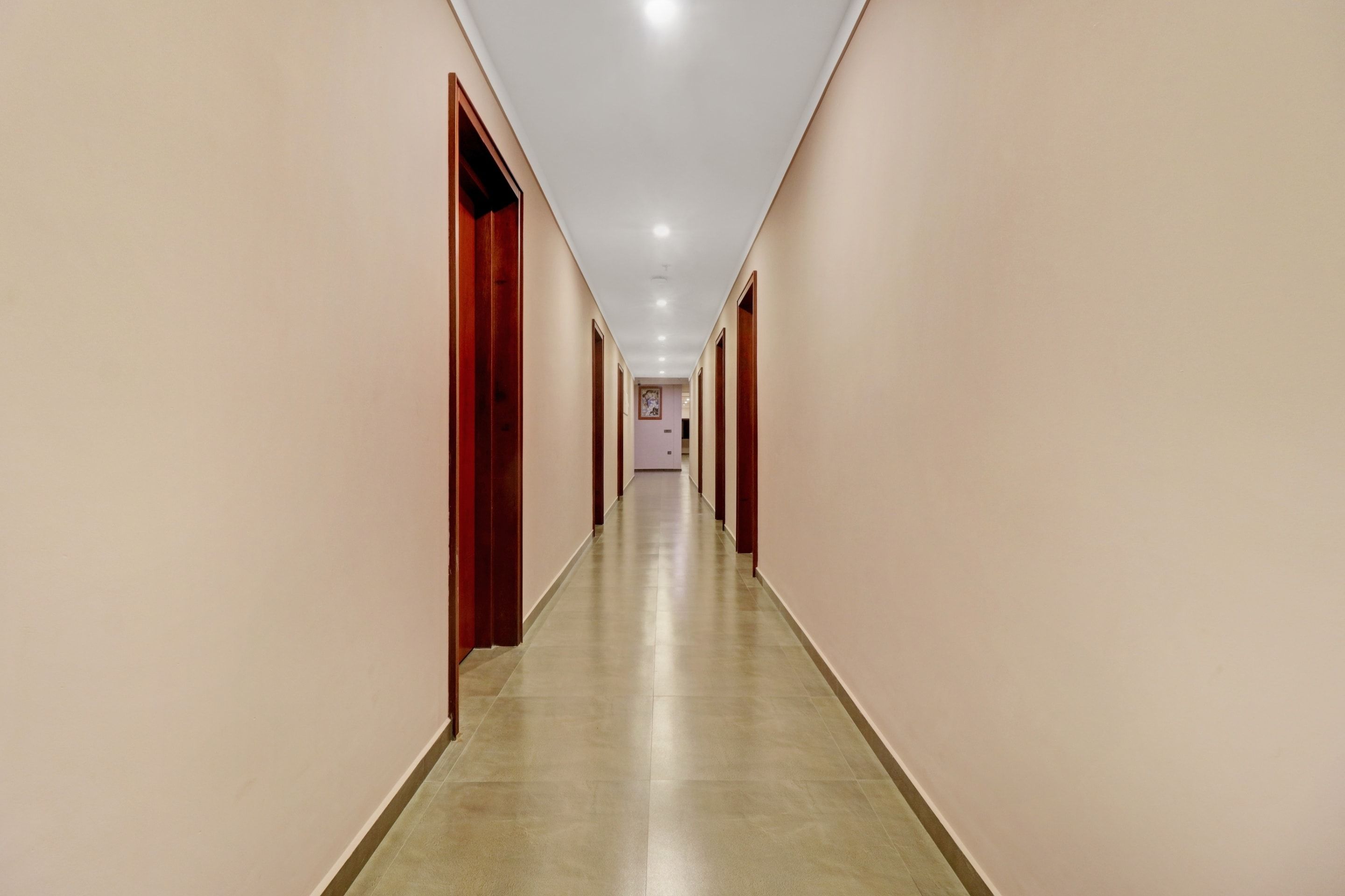 Un pasillo largo y estrecho con suelo de baldosas y puertas de madera a ambos lados.