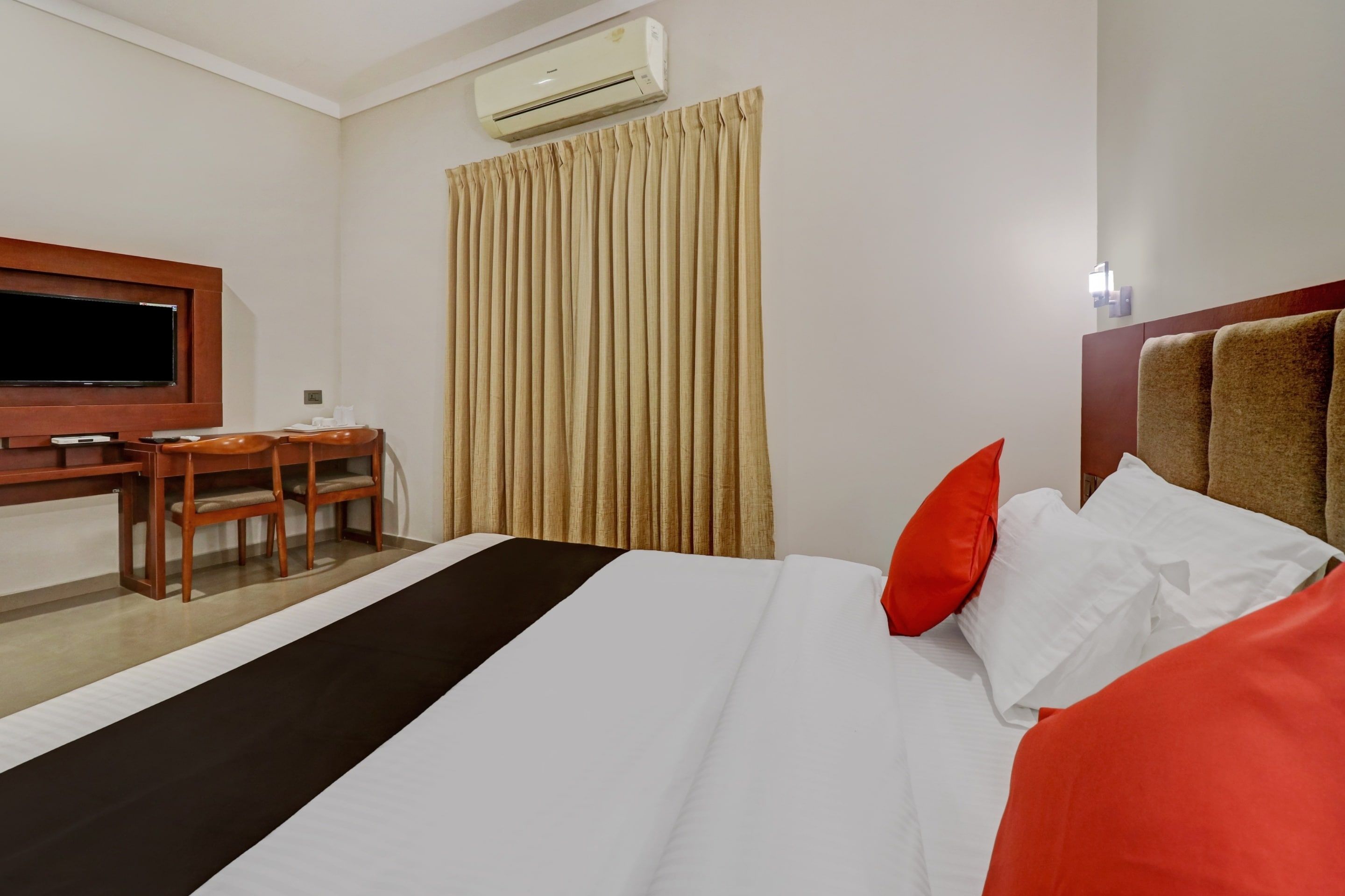 Habitación de hotel con cama, escritorio, silla, equipo de aire acondicionado y ventana con cortinas.