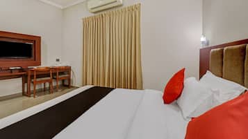 Habitación de hotel con cama, escritorio, silla, equipo de aire acondicionado y ventana con cortinas.