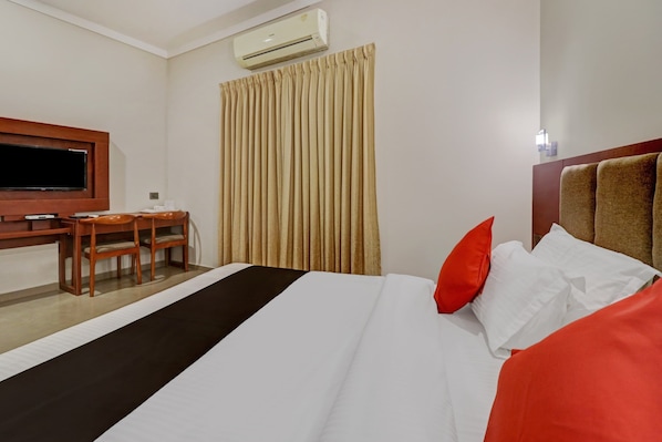 A hotel room with a bed, a desk, a chair, an air conditioning unit, and a window with curtains.