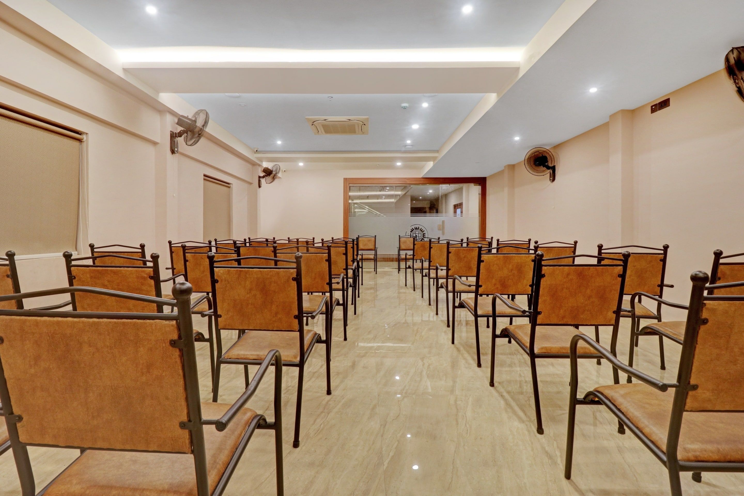 Un salón de conferencias de hotel con filas de sillas, un ventilador de techo y una puerta al fondo.
