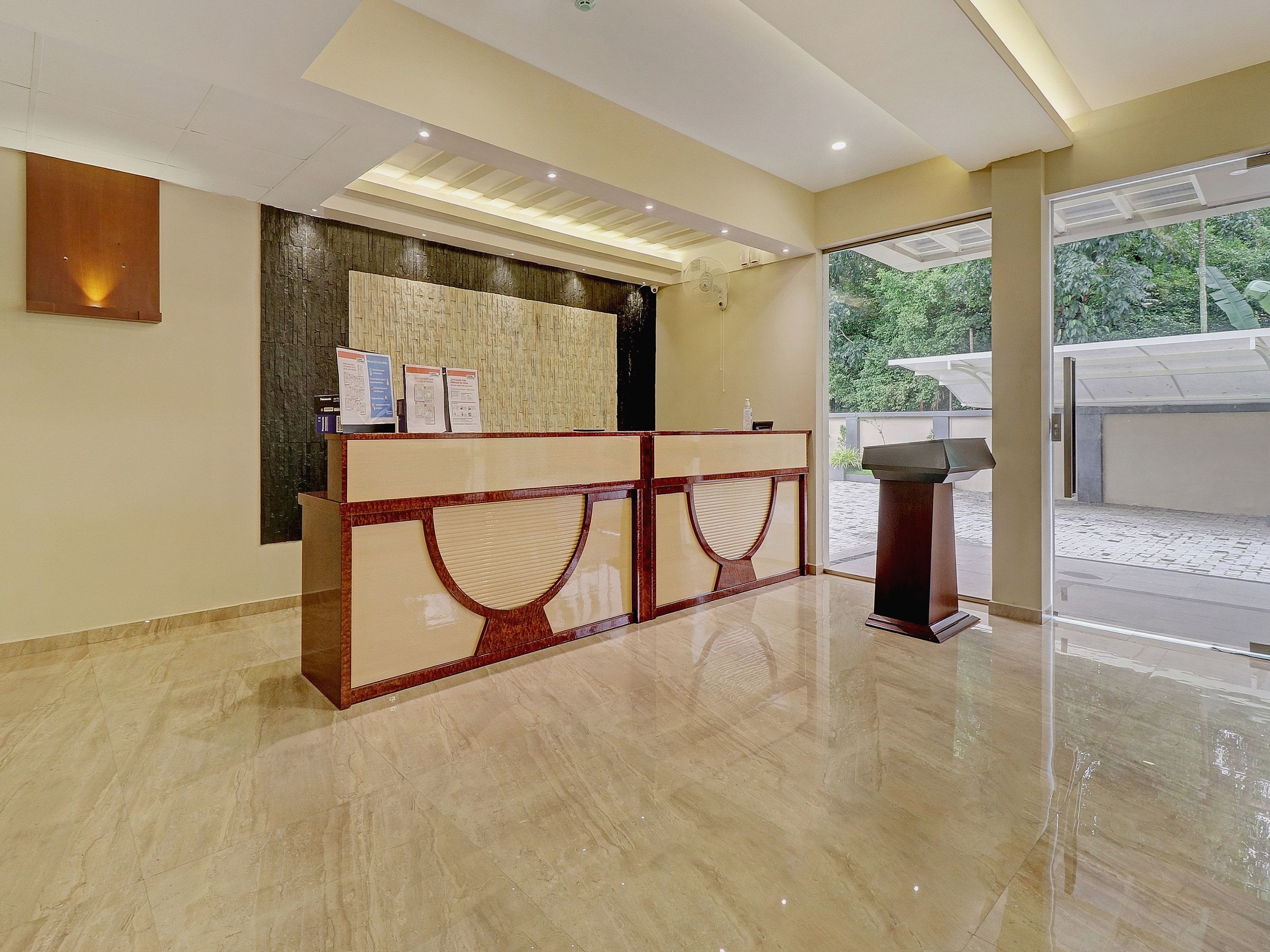 A reception area with a marble floor, a reception desk, and a view of greenery outside.