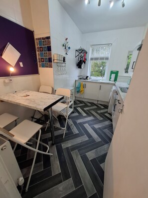 A modern kitchen with a dining area, featuring a marble countertop, white cabinets, and a herringbone floor pattern. - Spacious, quiet 2 bedroom garden flat sleeps 4 (Coatbridge)