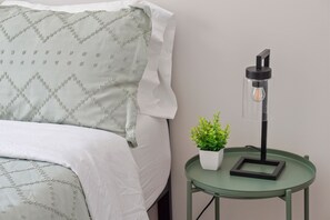 A bed with a patterned pillow and a bedside table with a lamp and a potted plant. - 13 mins to Campbell University Boho Retreat (Angier)